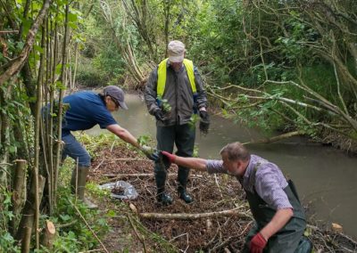 three people planting at the river edge