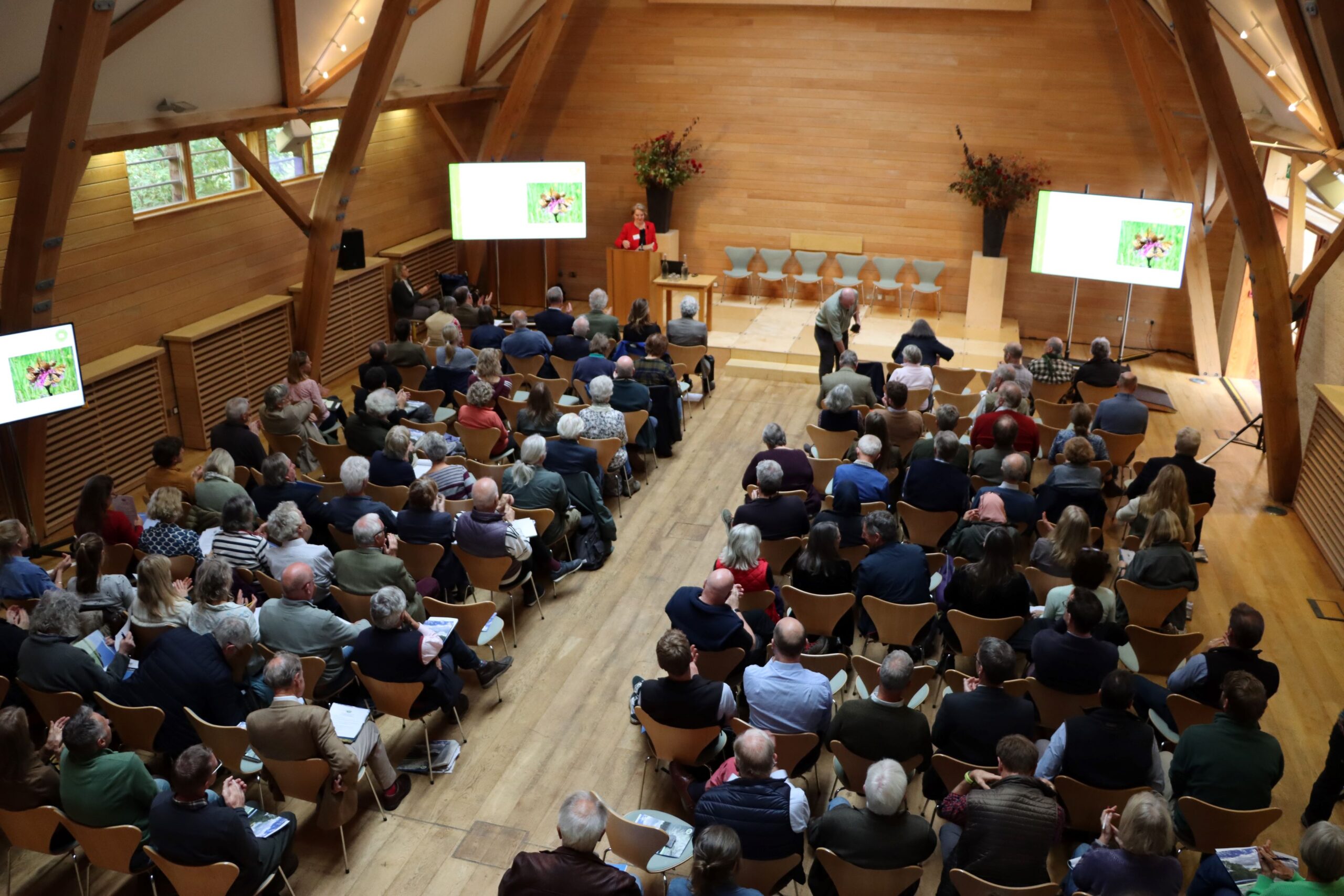 People sitting in a conference hall looking towards a speaker and display screens