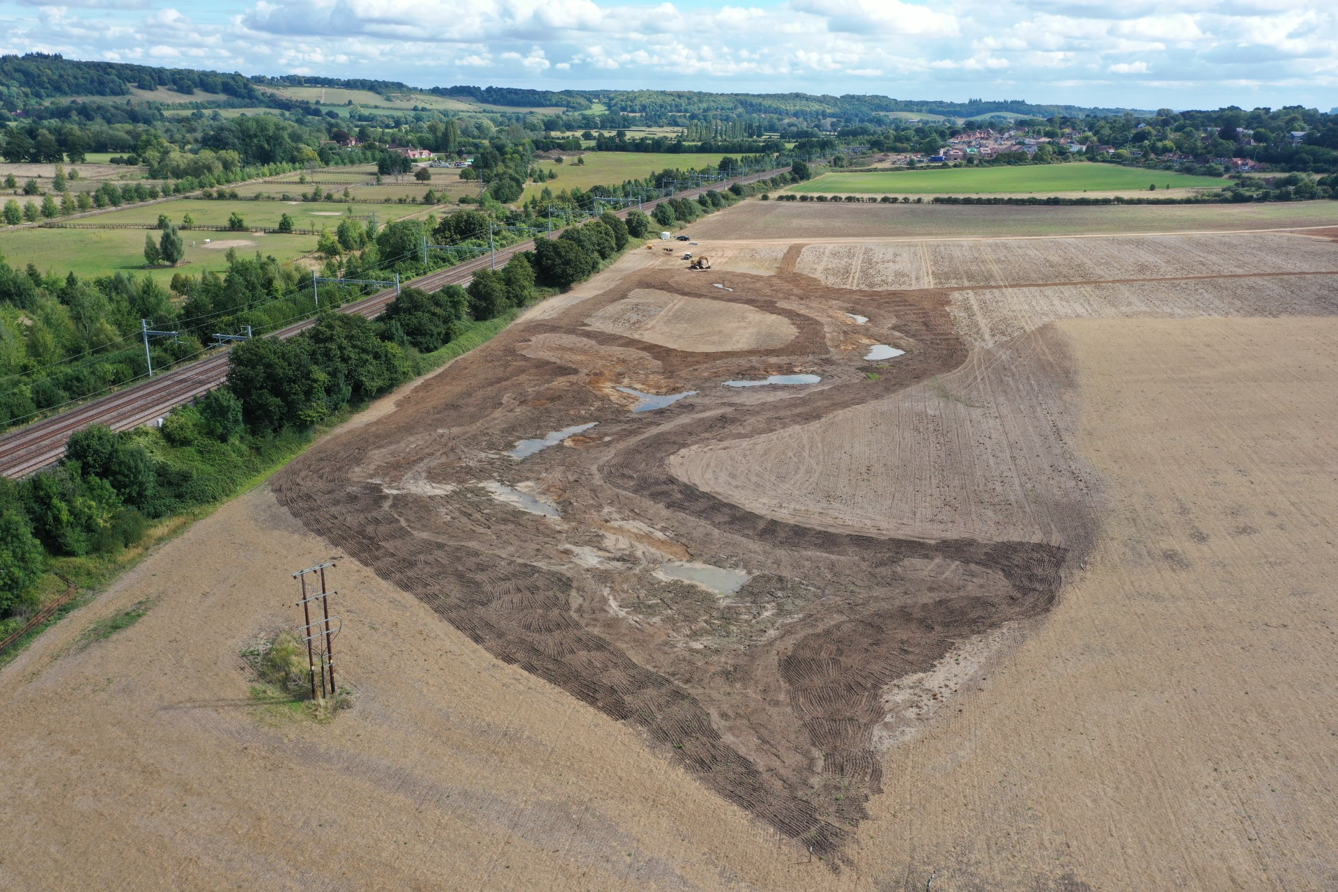 An aerial view of landscaping in a bare brown field. The field is next to a rail line