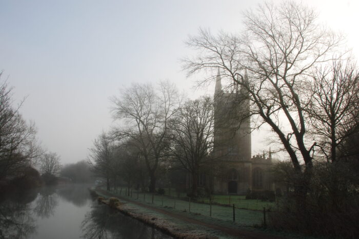 A church next to a canal on a foggy winter day.